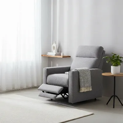 A modern grey fabric wall hugger recliner chair against a light wall in a minimalist small living room with a green plant